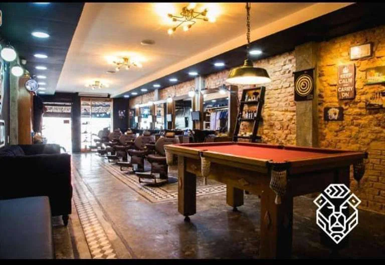 Fotografia do salão, com estações de atendimento, mesa de sinuca e tijolos aparentes.